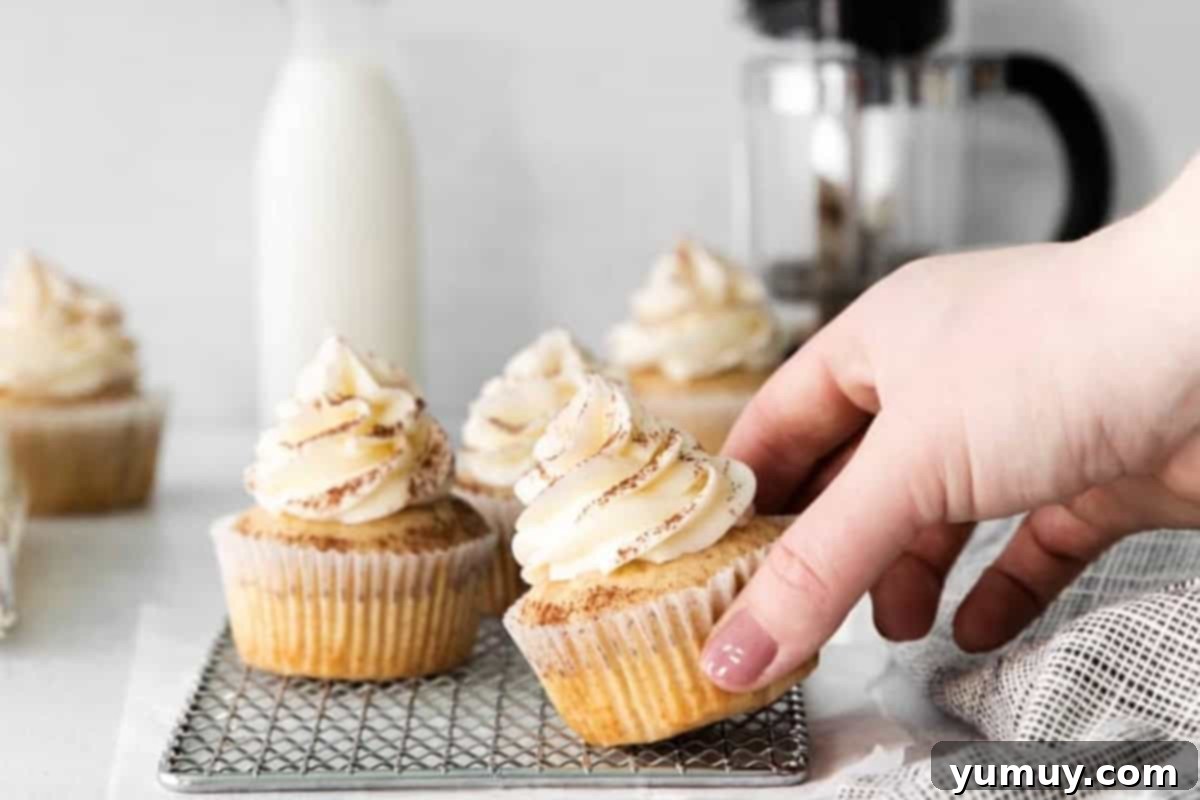 Decadent Tiramisu Cupcakes 3 a hand grabbing a tiramisu cupcake from a wire cooling rack.