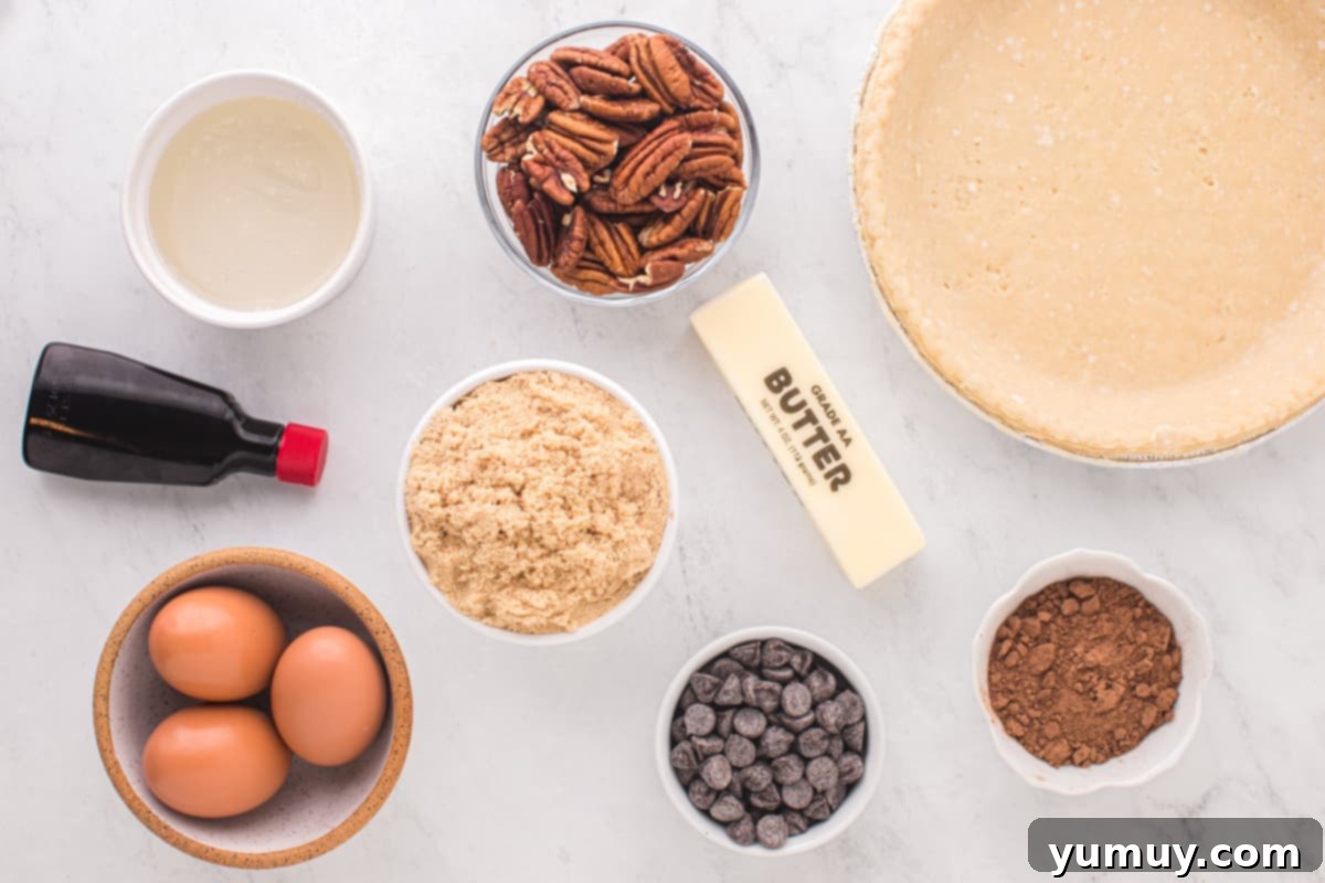 Overhead view of all the raw ingredients for chocolate pecan pie neatly arranged on a white surface, including eggs, brown sugar, corn syrup, vanilla, butter, cocoa powder, pecans, and chocolate chips.