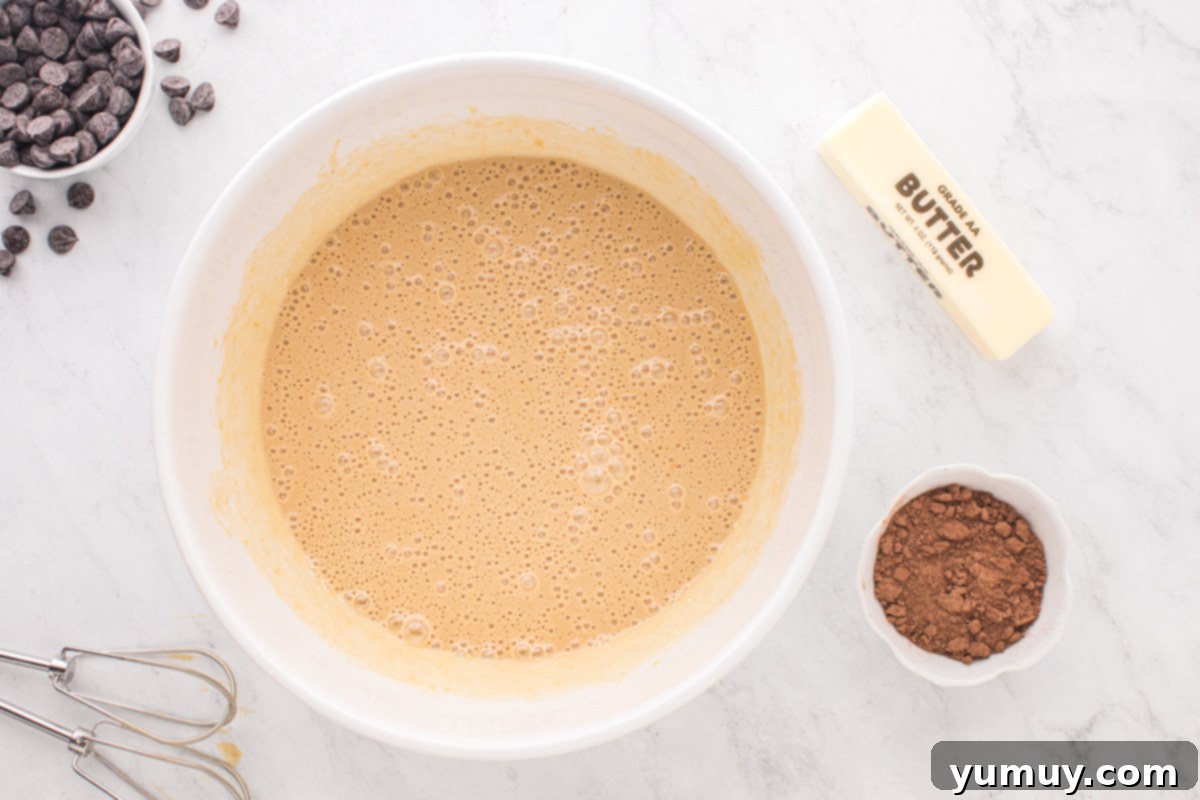 The smooth pecan pie base mixture, now incorporating corn syrup and vanilla extract, in a white mixing bowl.