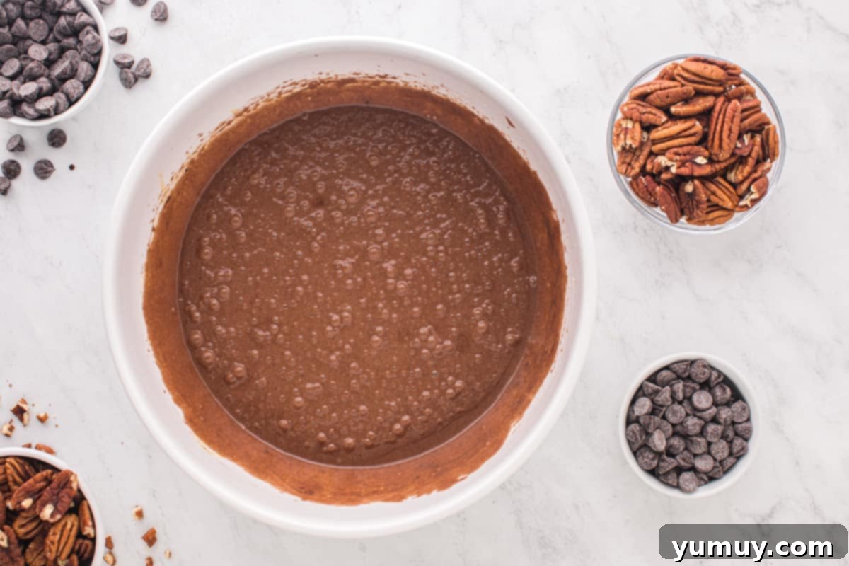 The chocolate and egg mixtures fully combined to form the rich chocolate pecan pie filling in a white mixing bowl.
