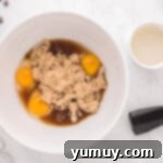 Eggs and brown sugar being beaten together in a white stand mixer bowl, creating a light, frothy mixture.