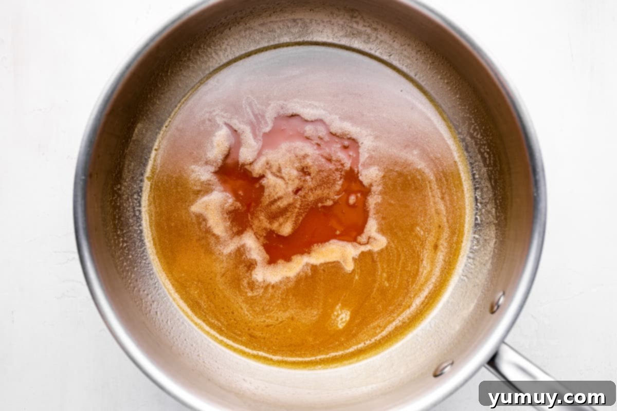 Flaky Pie Crust Apple Delights 15 Apple dumpling sauce simmering in a saucepan, showing its rich, brown color.