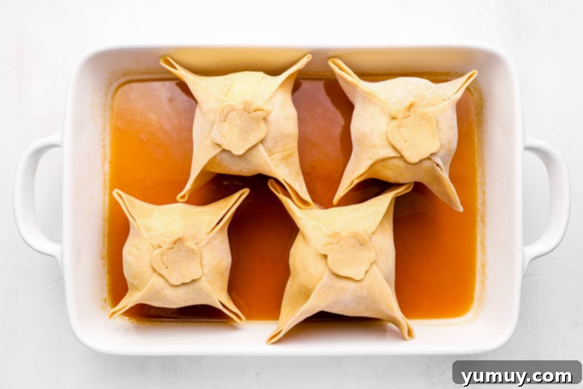Flaky Pie Crust Apple Delights 16 Apple dumplings baking in a pan with bubbling sauce, golden brown and ready to be removed from the oven.