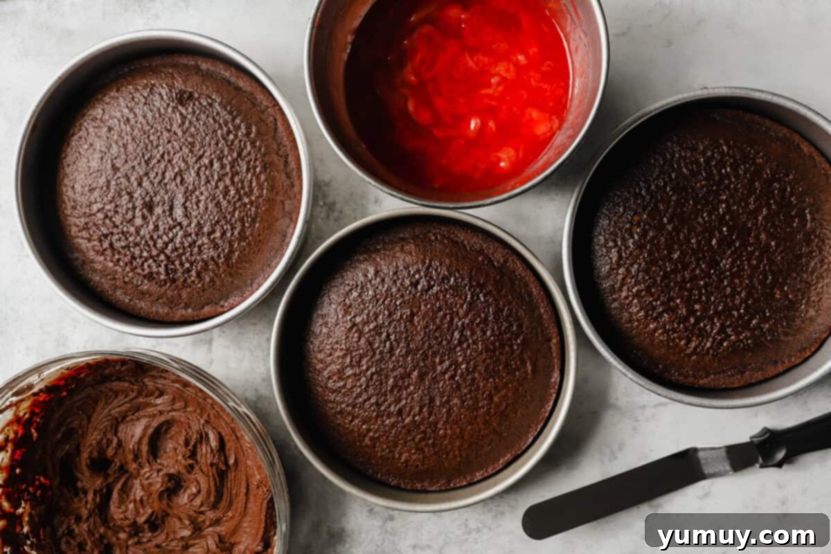 Decadent Chocolate Strawberry Delight 11 An overhead shot showcasing three beautifully baked chocolate cake layers cooling on a wire rack, flanked by bowls of vibrant strawberry filling and creamy chocolate frosting, awaiting assembly.