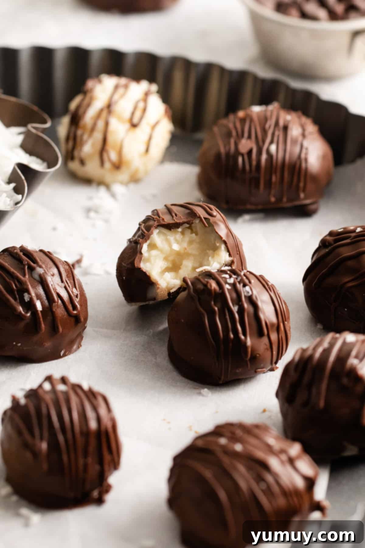 Creamy Coconut Delights 2 A perfectly bitten chocolate coconut truffle, revealing its creamy white coconut interior, on a serving dish filled with more delicious truffles.