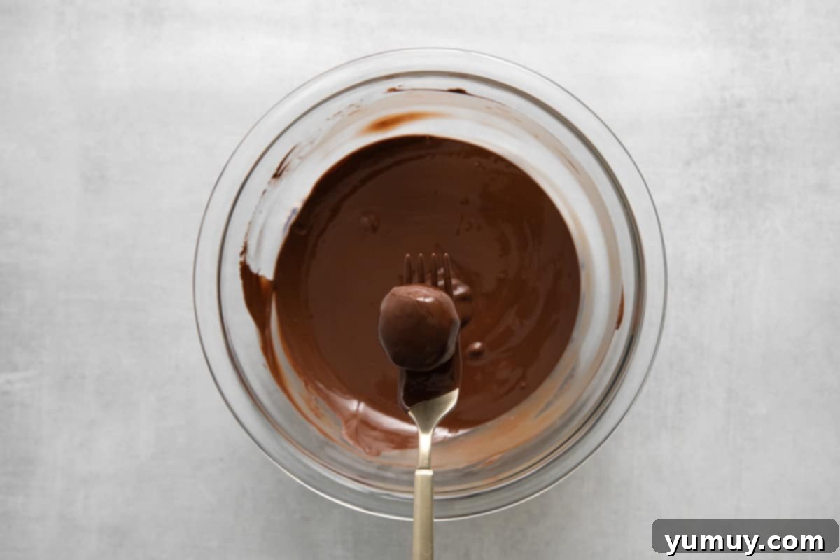 Creamy Coconut Delights 9 A fork carefully holding a chocolate-dipped coconut truffle over a bowl of rich, melted chocolate, allowing excess to drip away.