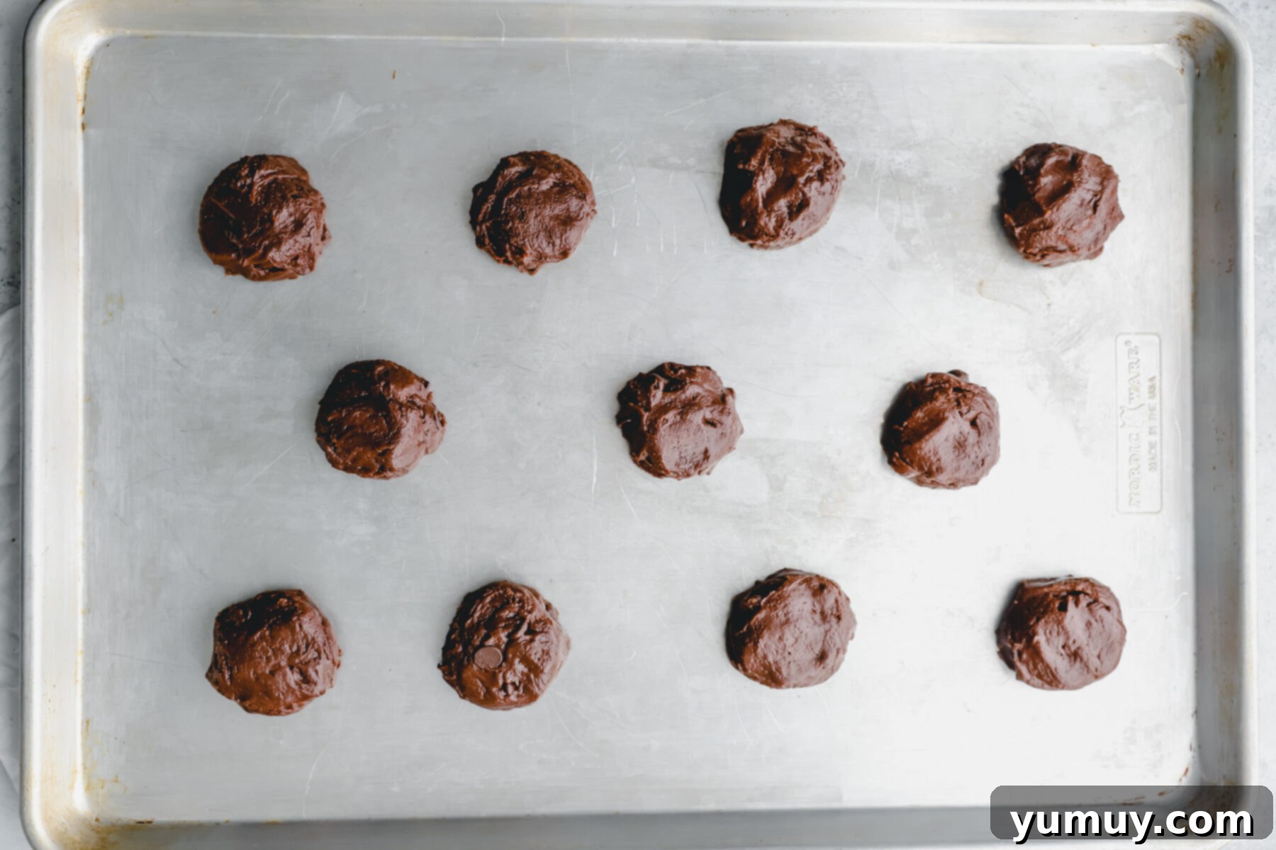11 cosmic brownie cookie dough balls on a baking sheet.