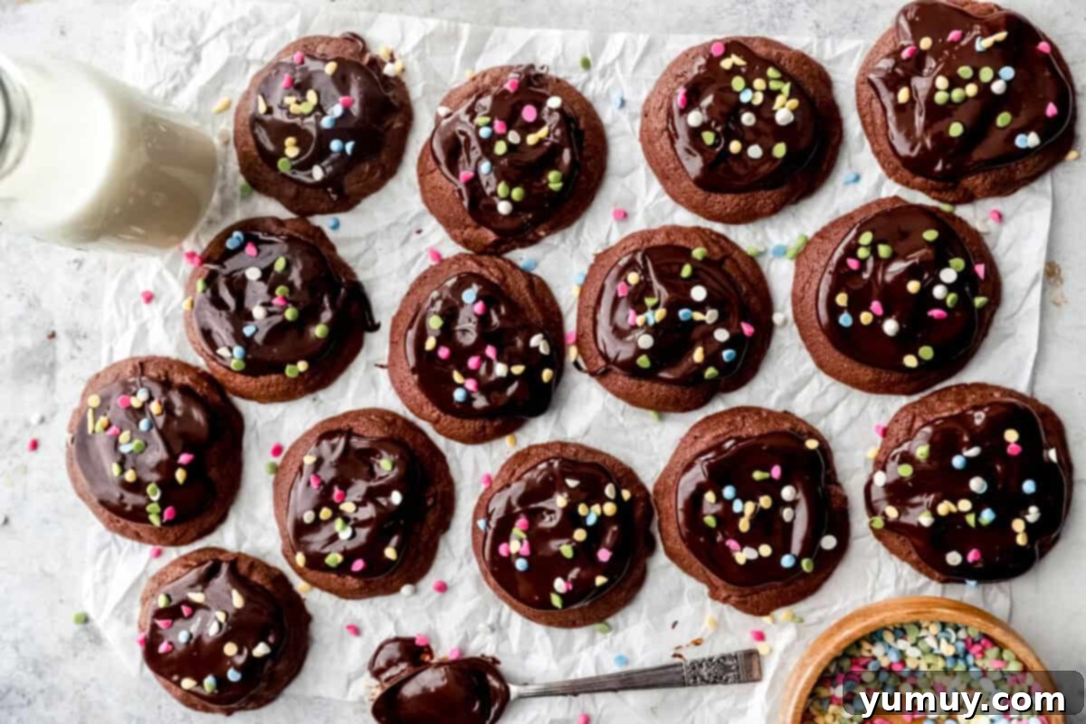 14 cosmic brownie cookies on parchment paper with a ganache coated spoon.