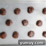 11 cosmic brownie cookie dough balls on a baking sheet.