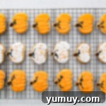 frosted pumpkin sugar cookies lined up on a cooling rack