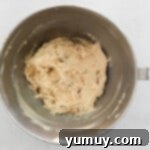 pecans folded into maple biscotti dough in a stainless mixing bowl.