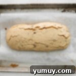 partially baked maple pecan biscotti loaf on a baking sheet.