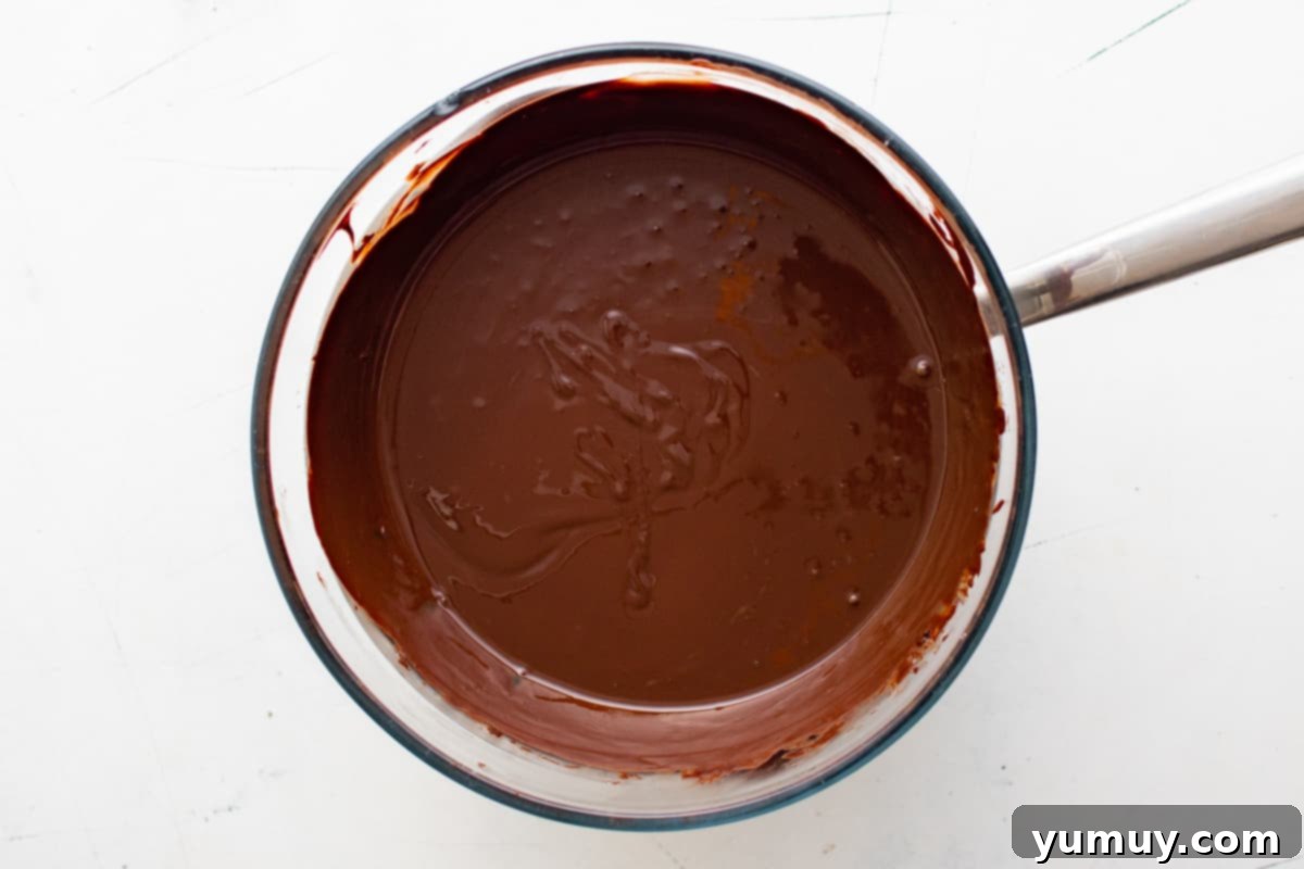Overhead view of dark and semisweet chocolate melting smoothly in a glass bowl over a double boiler, with a spoon stirring.