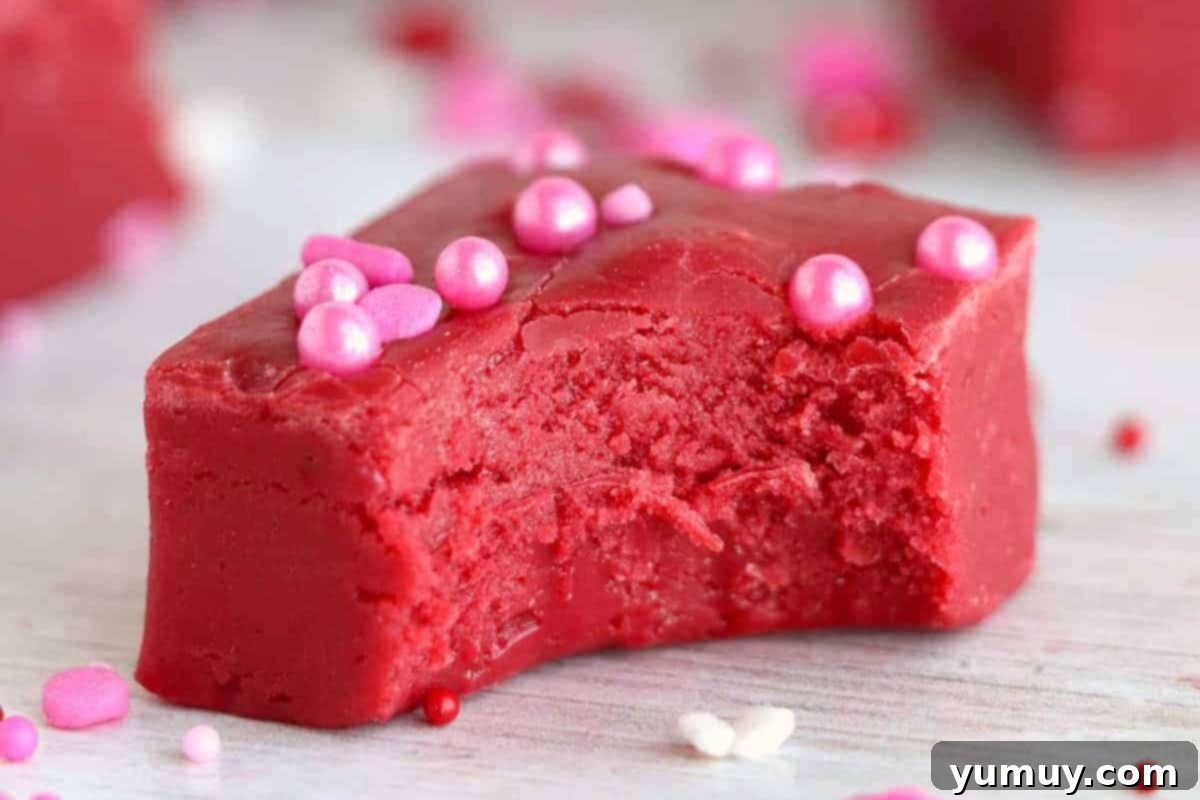 closeup of a bitten piece of red velvet fudge topped with pink sprinkles.