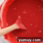 red velvet fudge mixture in a glass bowl with a wooden spoon.