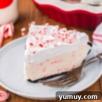 Frosty Peppermint Delight 5 A close-up of a slice of peppermint pie on a white plate with a fork, ready to be enjoyed.
