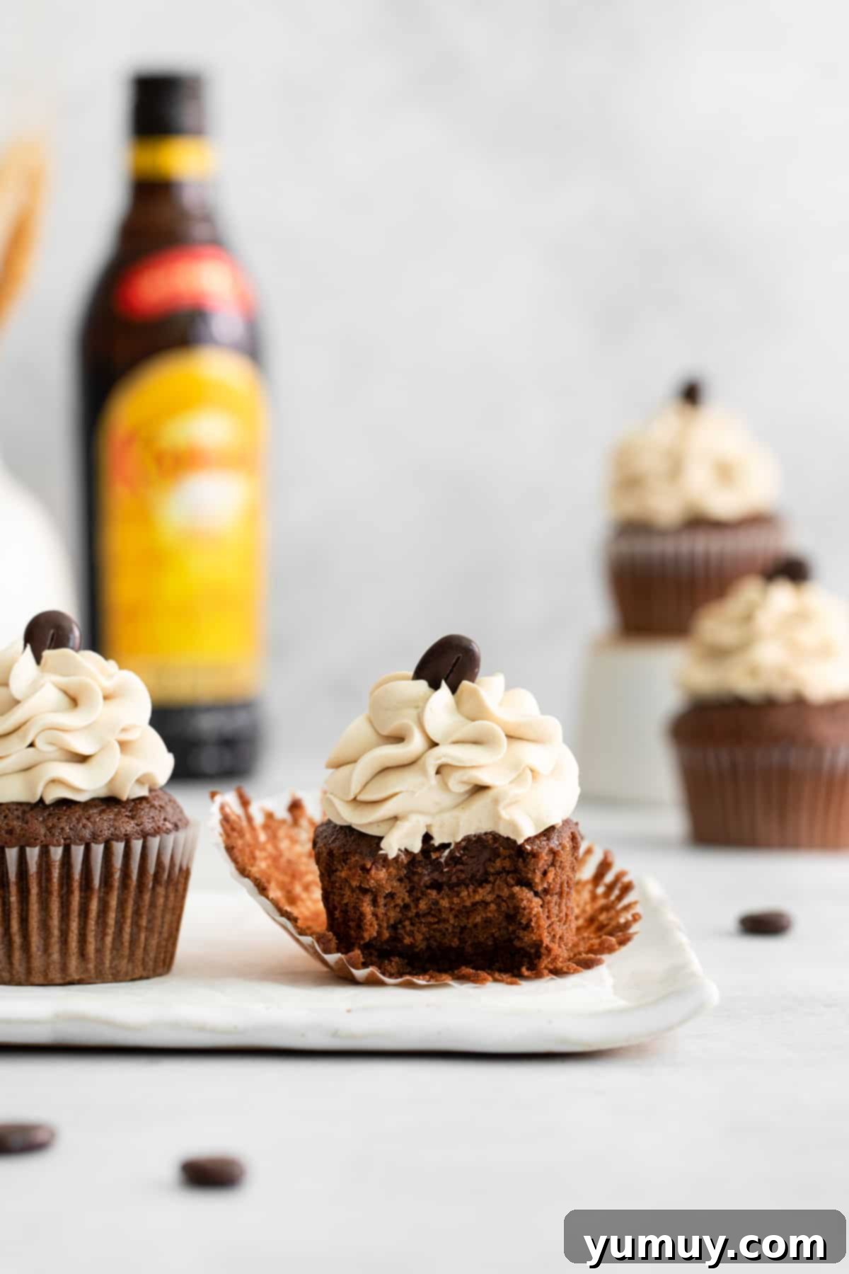 An unwrapped, bitten Kahlua cupcake sits on a rectangular white plate next to a perfectly wrapped Kahlua cupcake, highlighting the delicious ganache filling.