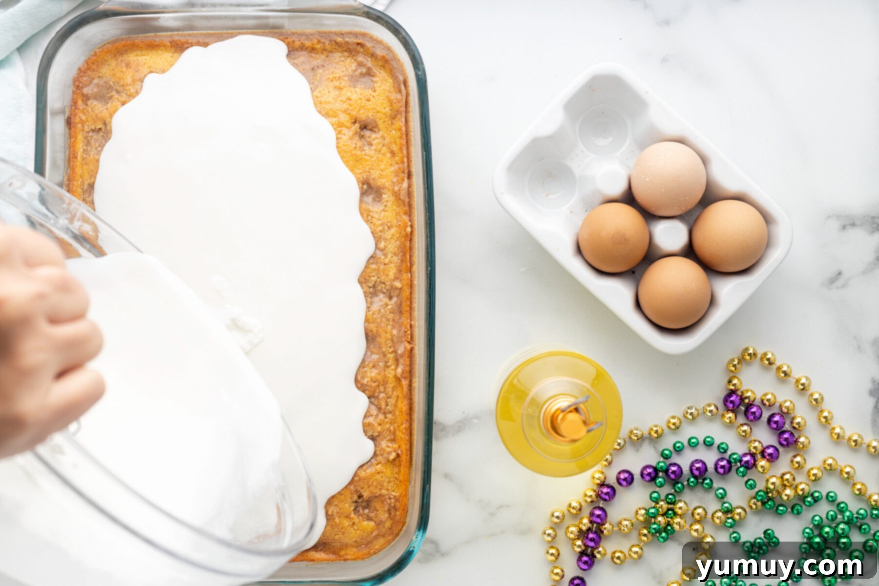 Mardi Gras King Cake Poke 18 A glistening white glaze being poured and smoothly spread over the top of the chilled King Cake Poke Cake in its baking pan.