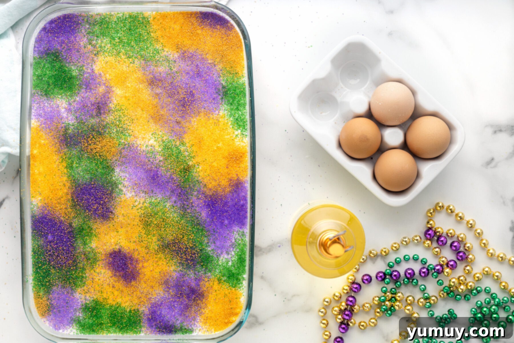 Mardi Gras King Cake Poke 19 The fully decorated King Cake Poke Cake, adorned with vibrant stripes of green, gold, and purple decorating sugars over its smooth white glaze, ready for serving.