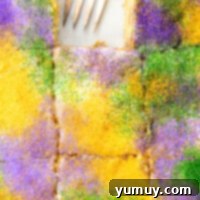 Mardi Gras King Cake Poke 5 A close-up view of a sliced King Cake Poke Cake, with one festive slice removed and a fork nearby, showcasing its rich texture and vibrant Mardi Gras sprinkles.