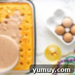 Mardi Gras King Cake Poke 8 A luscious cinnamon pudding mixture being poured generously over the poked yellow cake in a rectangular baking pan, visibly filling the holes.