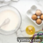 Mardi Gras King Cake Poke 10 A perfectly smooth white glaze for King Cake Poke Cake in a clear glass bowl, with a whisk demonstrating its ideal pourable consistency.