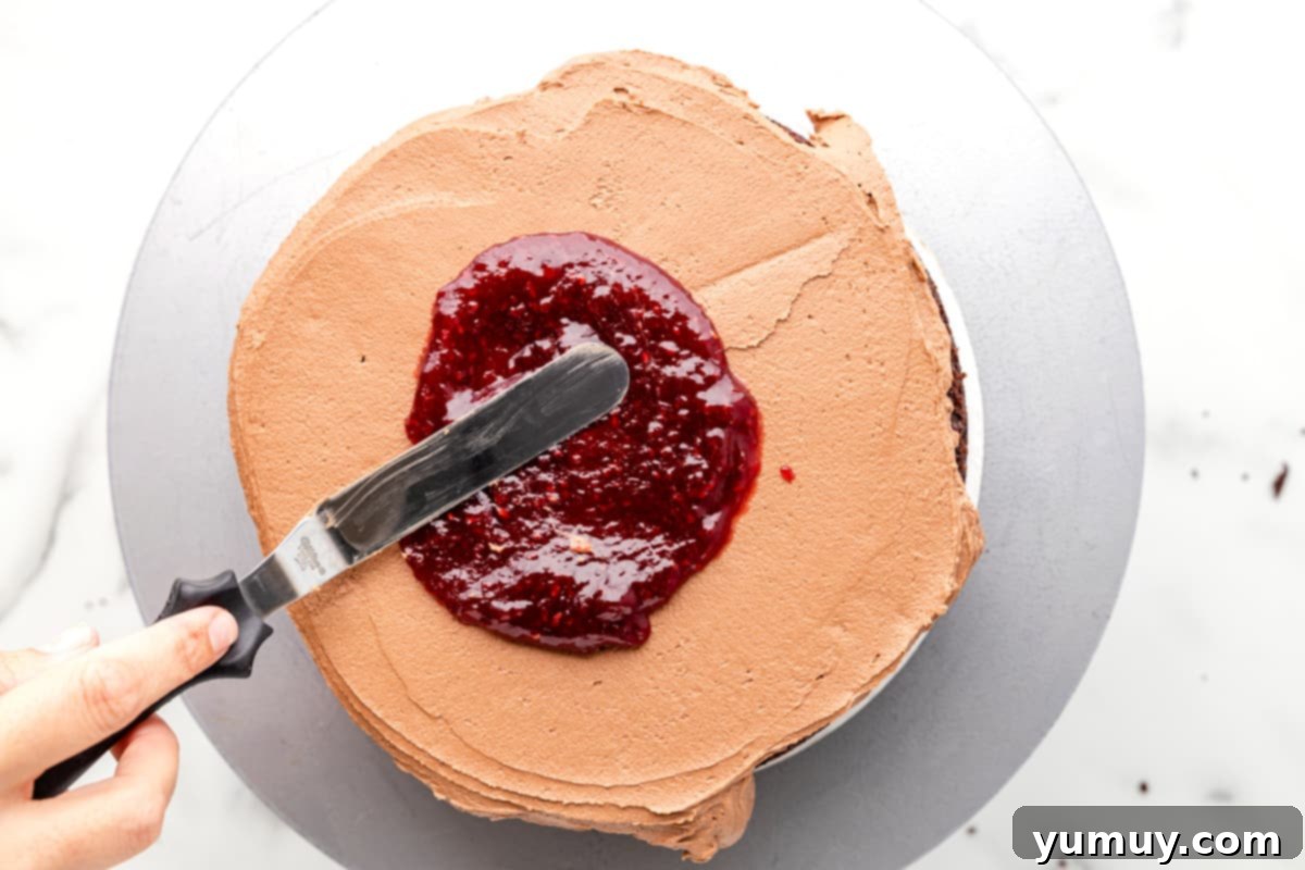 Dark Chocolate Raspberry Gateau 15 raspberry preserves spread over chocolate frosting and chocolate cake on a gray cake board.