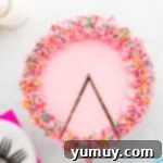 overhead view of a cake server removing a slice from a pink frosted doctored white cake mix cake, adorned with sprinkles.