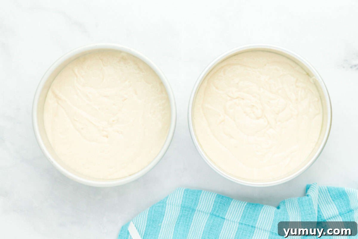 doctored white cake mix batter perfectly portioned into round baking pans, ready for the oven.