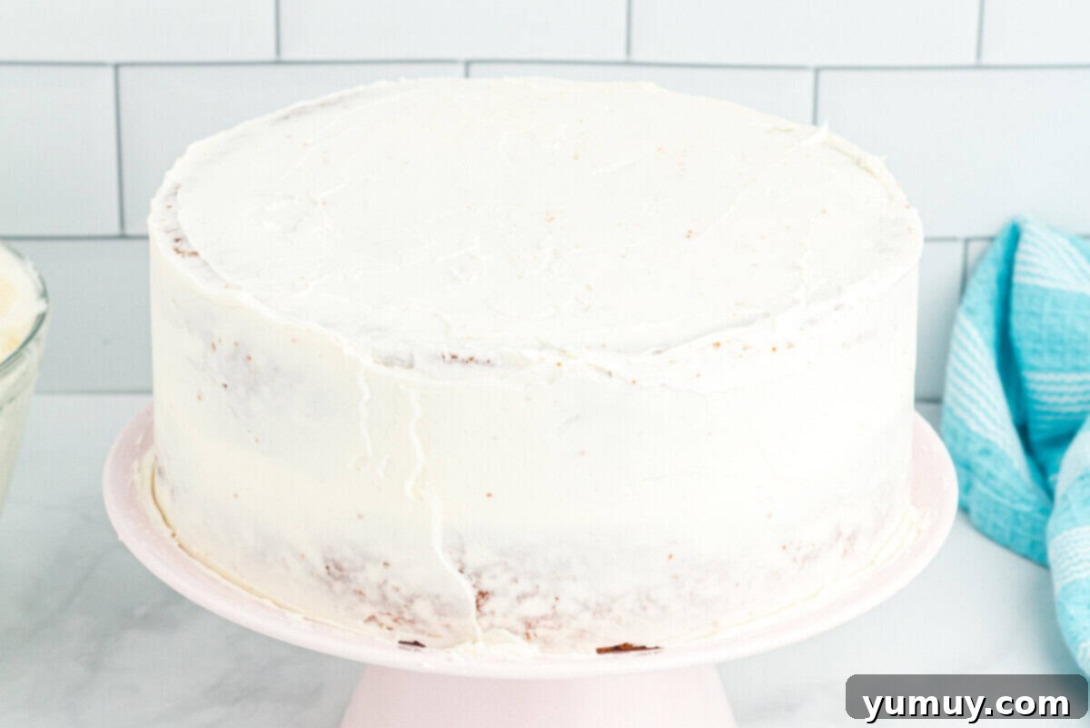 a perfectly crumb-coated doctored white cake mix cake on a white cake stand, prepared for its final layer of frosting.