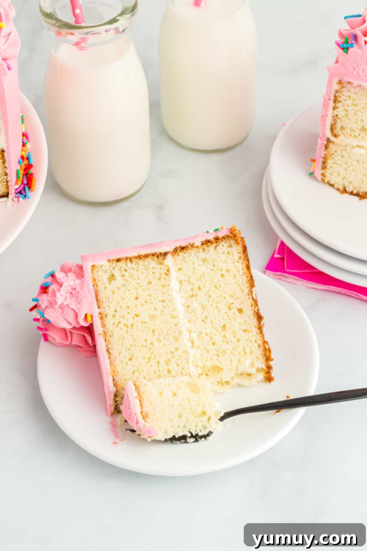 a forkful of moist doctored white cake mix cake resting on a white plate next to a beautifully frosted slice.