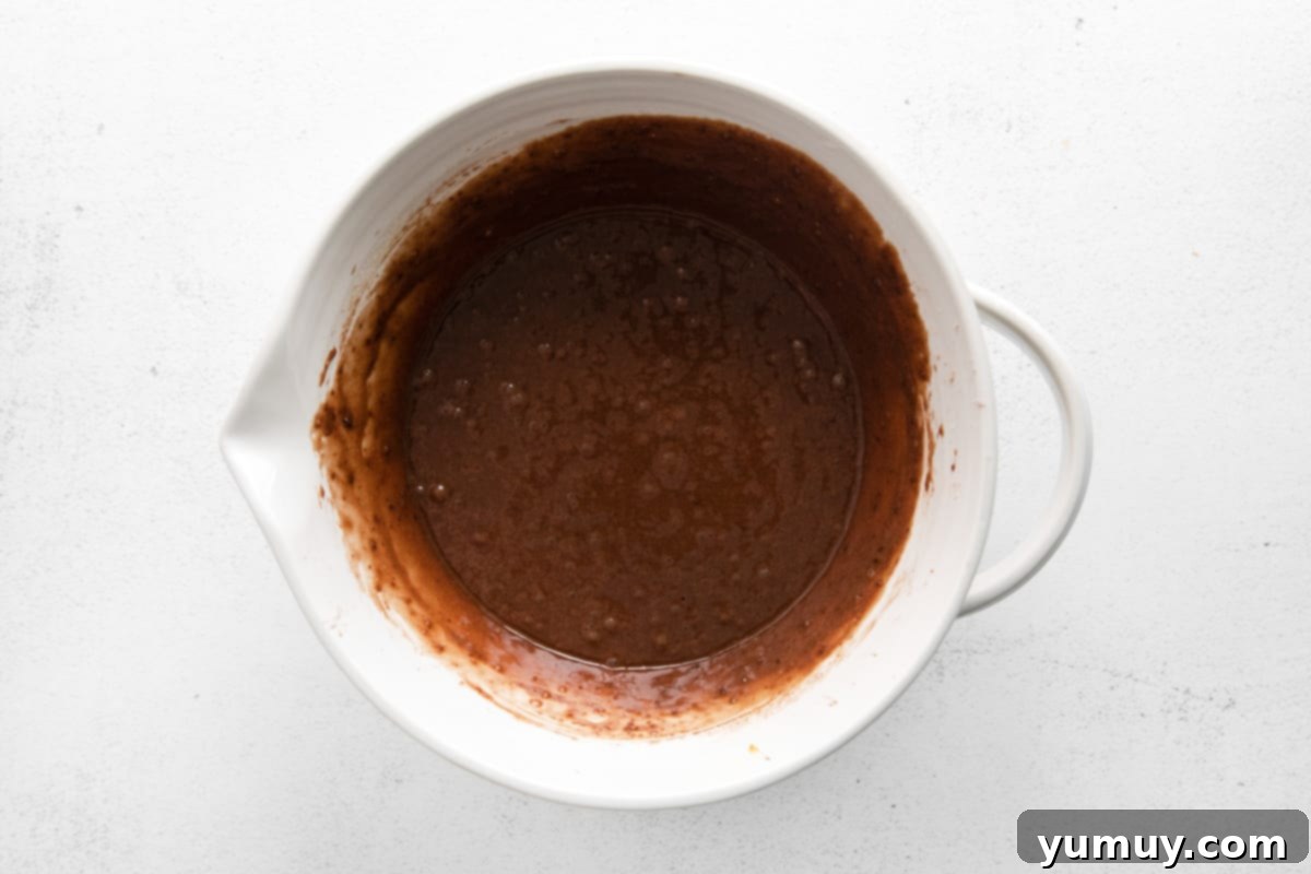 Smooth and glossy chocolate cupcake batter in a white mixing bowl, ready to be portioned for baking.