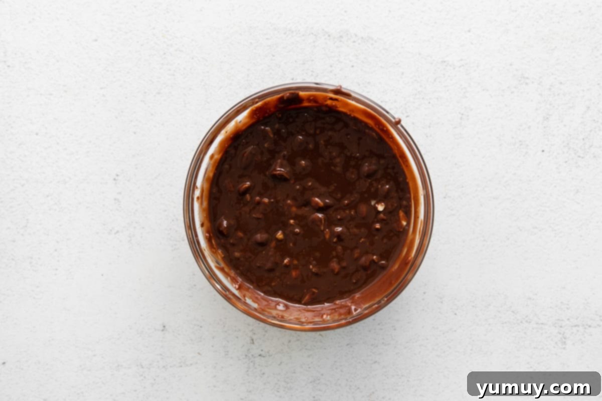 A small glass bowl containing rich chocolate ganache mixed with crunchy, finely chopped hazelnuts, prepared as the filling.