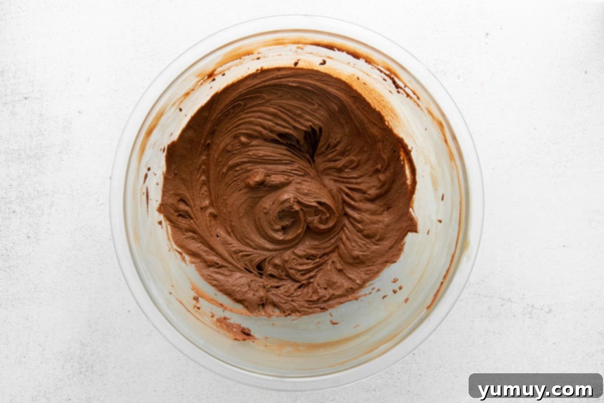 A clear glass bowl filled with perfectly whipped, light, and airy chocolate ganache frosting, ready for piping.