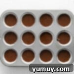 Cupcake batter carefully portioned into a 12-count cupcake tin lined with paper liners, ready for baking.