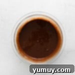 Smooth, rich chocolate ganache in a clear glass bowl after being stirred, perfectly emulsified.