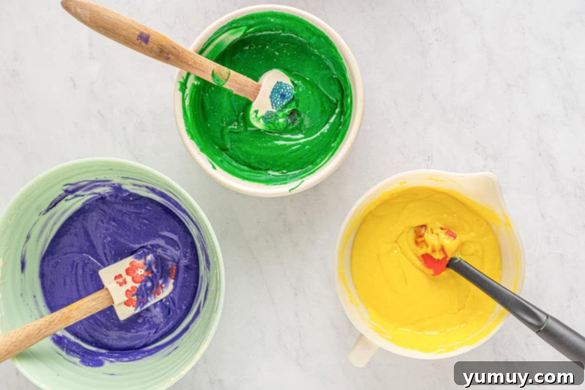 Mardi Gras Birthday Fiesta 16 Separate bowls of purple, green, and yellow Mardi Gras birthday cake batter, each mixed with a rubber spatula to achieve even color.