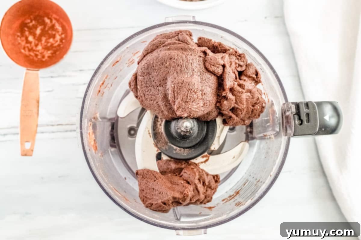 Thin Mint cookie dough, mixed with wet ingredients, forming a cohesive ball in the base of a food processor.