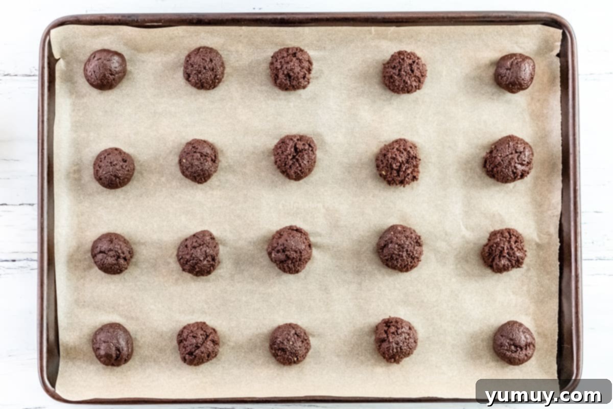 Twenty perfectly round Thin Mint cookie dough portions arranged on a parchment-lined baking sheet, ready for the oven.