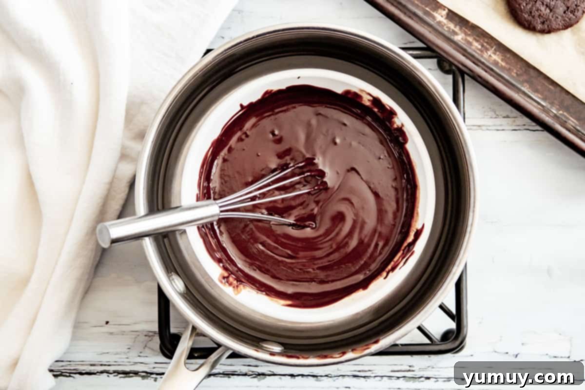 Melted chocolate mint coating in a bowl, being whisked to a smooth and glossy texture, ready for dipping the cookies.