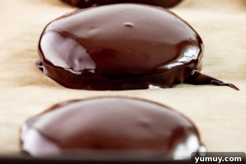 Close-up three-quarters view of a perfectly aligned row of three freshly dipped Thin Mint cookies on a baking sheet, with their shiny chocolate coating.