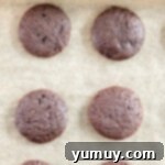 Close-up overhead view of perfectly baked Thin Mint cookies on a parchment-lined baking sheet, showing their dark, rich color.