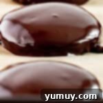 Close-up three-quarters view of a row of three freshly dipped Thin Mints on a baking sheet, with their glossy chocolate coating still setting.