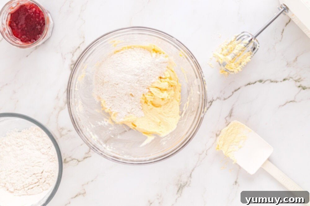 Heart Kiss Cookies 17 Dry ingredients (flour and cornstarch) for heart thumbprint cookies gradually added to the wet mixture in a glass bowl, with dough just starting to form.