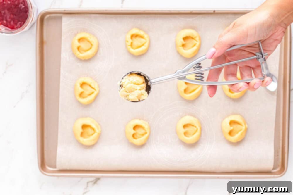 Heart Kiss Cookies 19 A hand using a cookie scoop to portion out dough onto a parchment-lined baking sheet, forming small, uniform cookie balls.