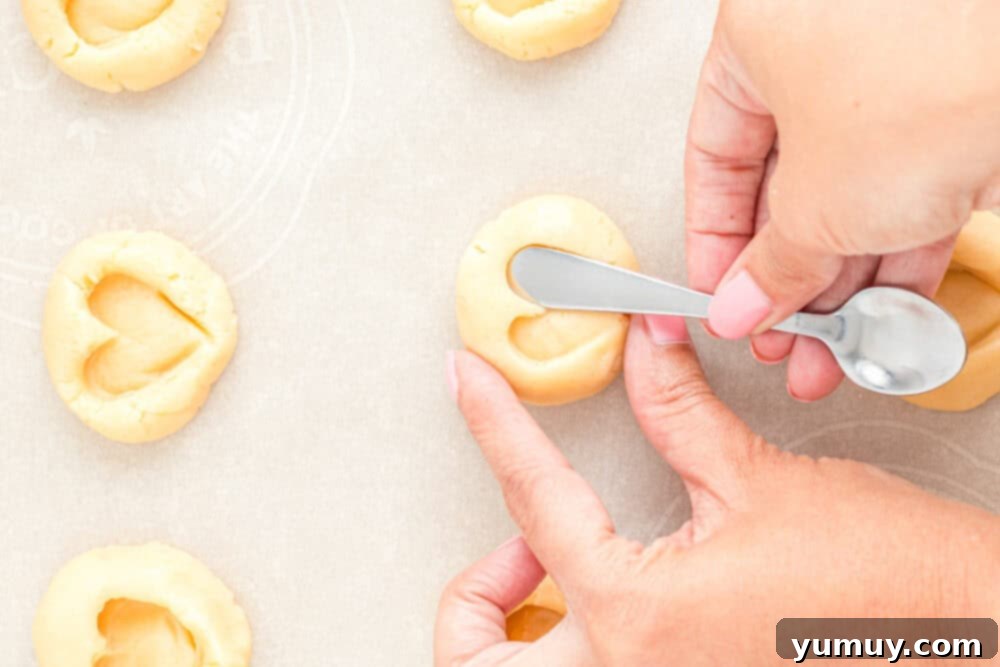 Heart Kiss Cookies 20 A hand gently pressing a heart shape into a cookie dough ball on a baking sheet, using a butter knife for a defined impression.