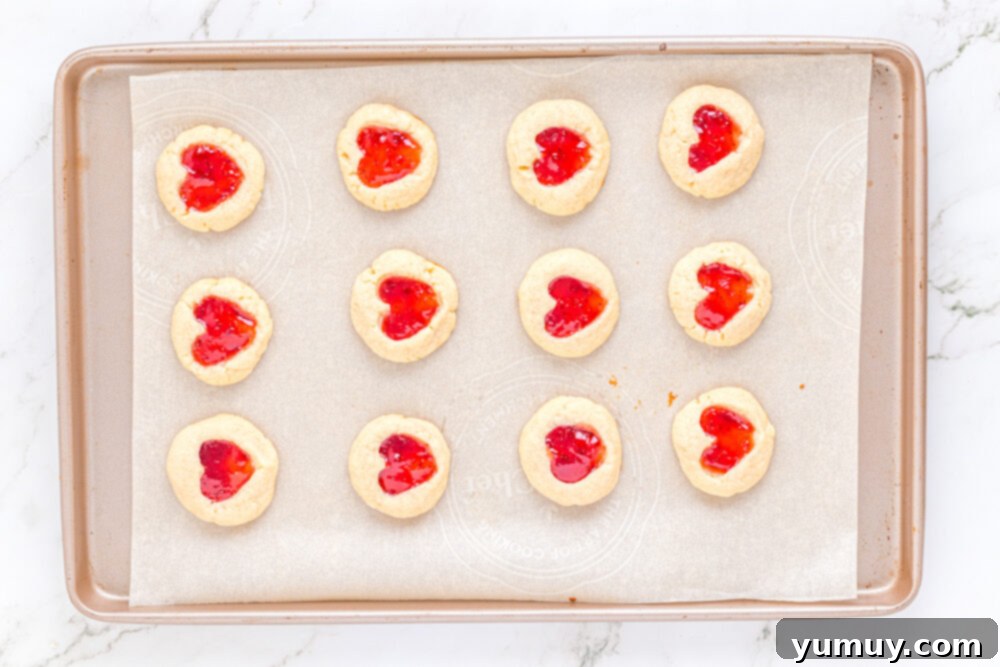 Heart Kiss Cookies 22 A baking sheet filled with 12 heart thumbprint cookies, freshly baked to a golden brown with bubbling jam centers.