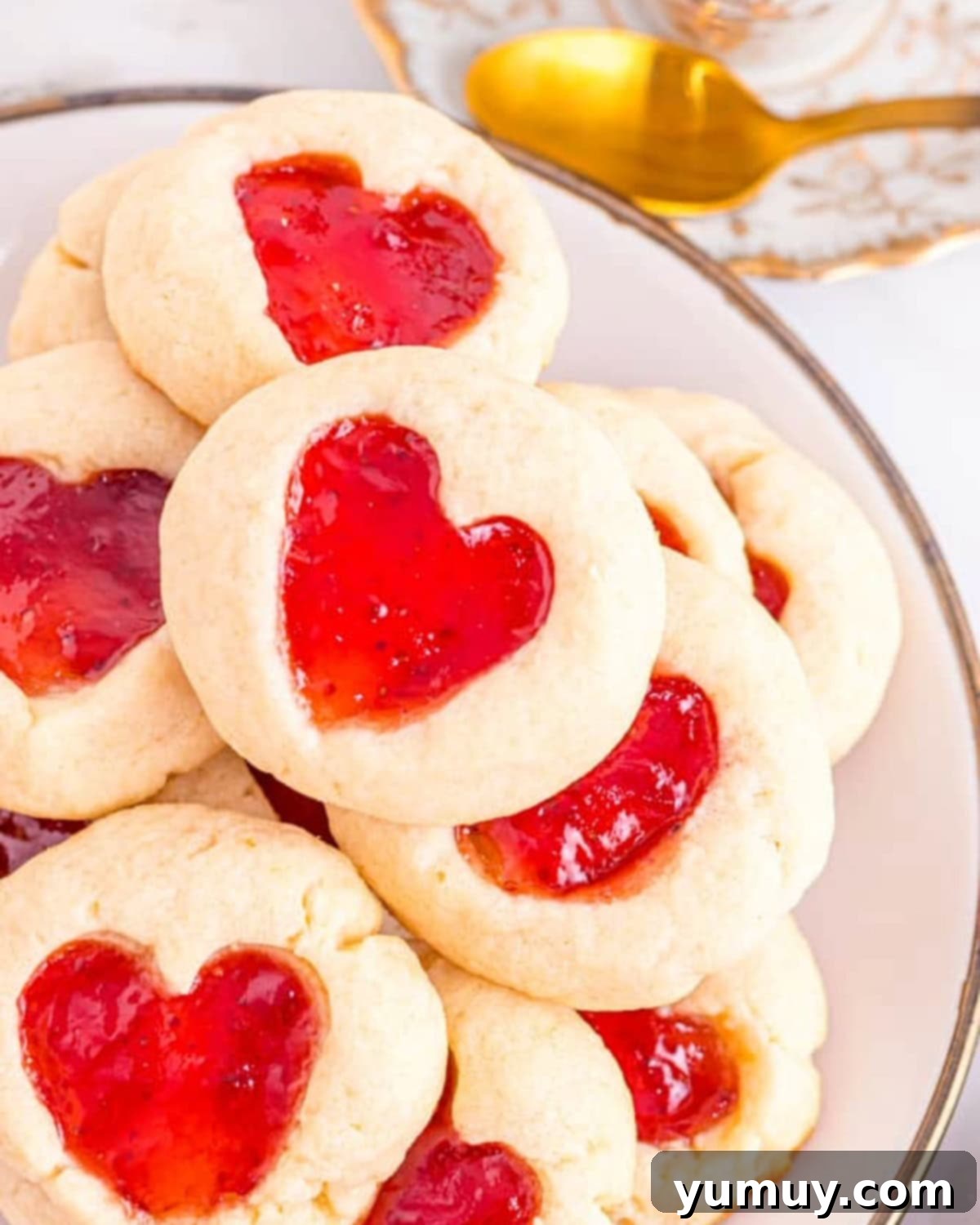 Heart Kiss Cookies 4 A plate filled with beautiful heart-shaped thumbprint cookies, each perfectly filled with vibrant red jam.