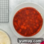 Two stacked layers of pink velvet cake with a generous layer of cream cheese frosting in between, on a white cake stand.