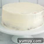 Side view of a pink velvet cake with a thin crumb coat of frosting applied, ready for the final layer.